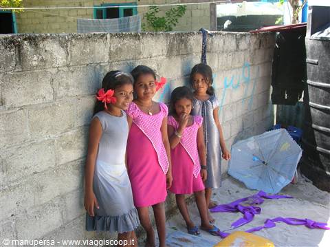 Four girls in grey and pink dresses by a concrete wall, umbrella open on the sand