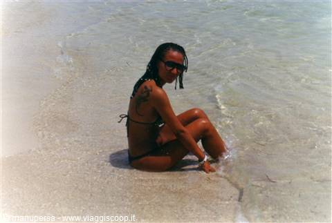 Girl in bikini sitting in clear shallow water on white sand beach