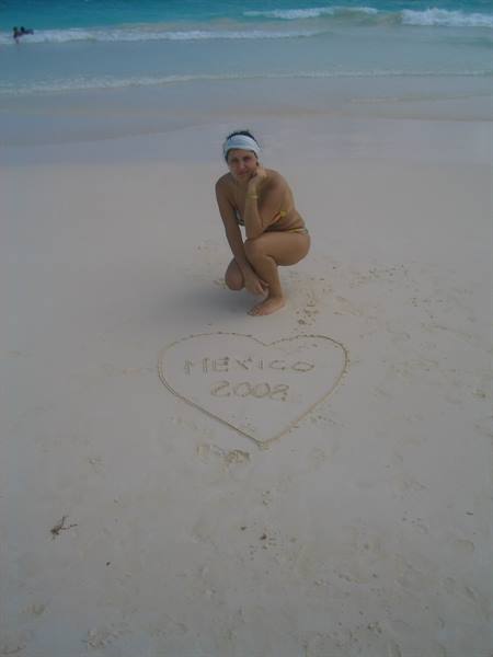Woman crouching on white sand next to a heart reading Mexico 2008