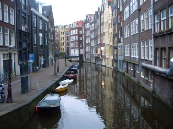 Boats moored along an Amsterdam canal between narrow houses under gray morning light