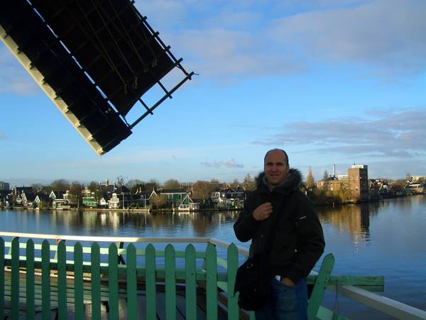 Man in front of a windmill sail at Zaanse Schans, river and houses behind