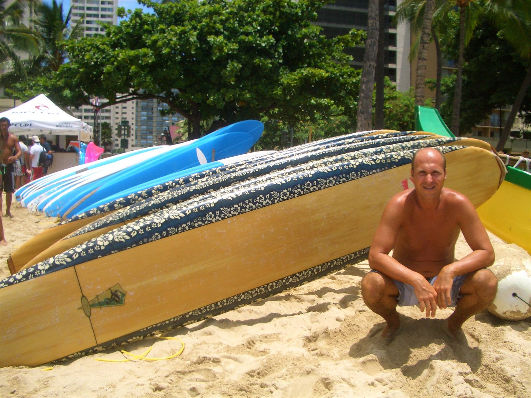 Man crouching beside wooden surfboards on the sand at Waikiki