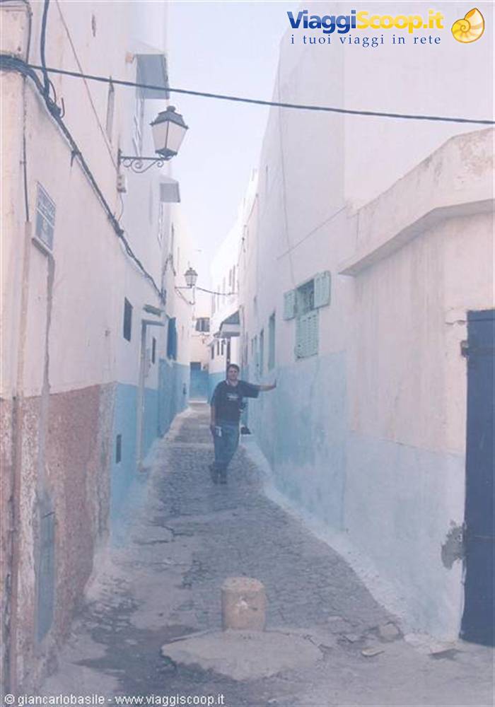 Man walks through cobblestone alley with white and blue walls in the Kasbah
