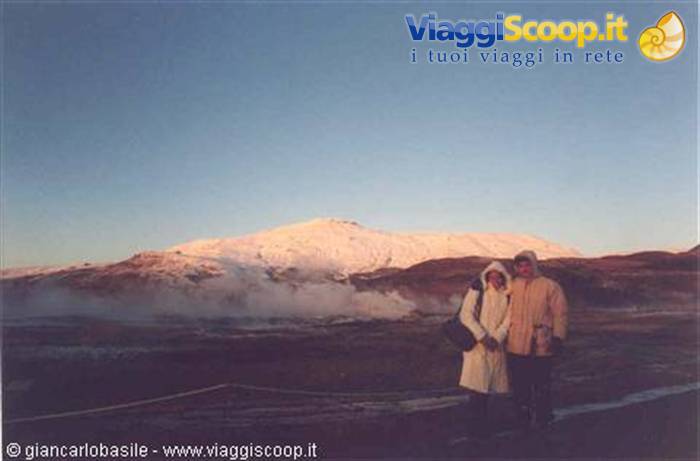 Couple in hoods beside geothermal steam under snowy mountain, Iceland