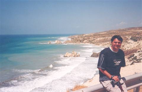 Smiling man in black shirt beside rocky coast with turquoise waves and white foam