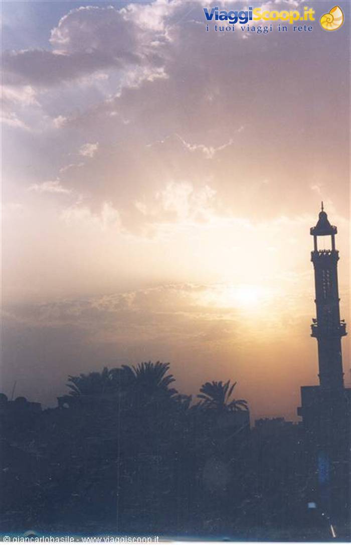 Minaret silhouetted against the low sun, dark palms below