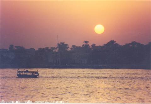 Boat on the Nile at sunset among palms and orange sky
