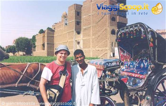 Tourist and driver beside a decorated horse carriage, in front of mud-brick buildings