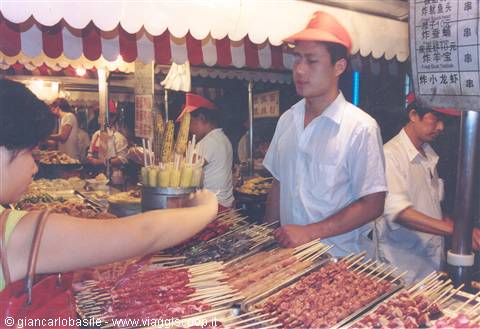 Vendor in red cap serving meat skewers at a night market stall