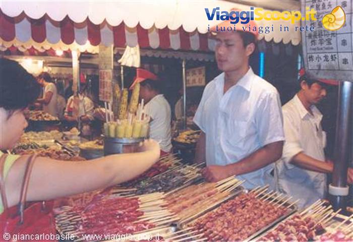 Vendor in red cap serving meat skewers at a night market stall