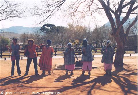 Herero women in traditional dresses dancing on red soil under a tree