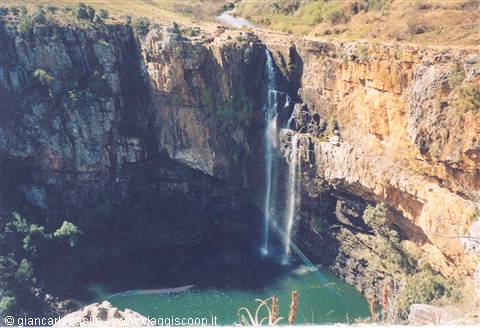  rocky waterfall drops into green pool between ochre cliffs