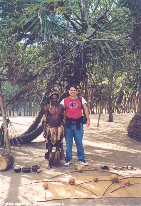 Tourist next to a man in traditional dress among palms and mats with instruments