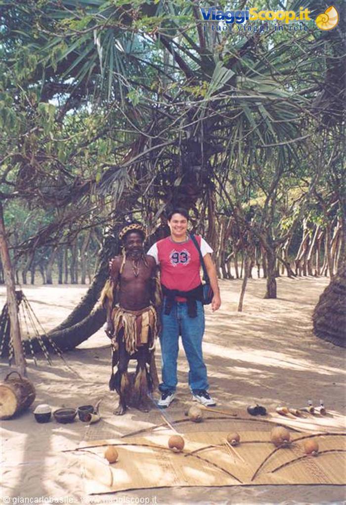 Tourist next to a man in traditional dress among palms and mats with instruments