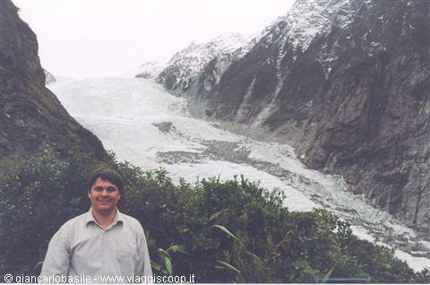 Man in shirt in front of Franz Josef Glacier between snowy rock walls