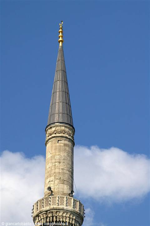Stone minaret with golden finial against blue sky and clouds