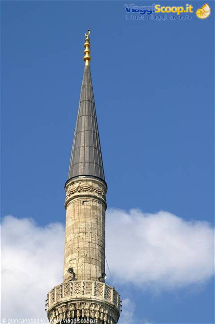 Stone minaret with golden finial against blue sky and clouds