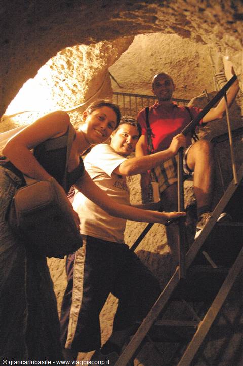 Tourists on metal staircase inside rock-hewn tunnel, warm lighting