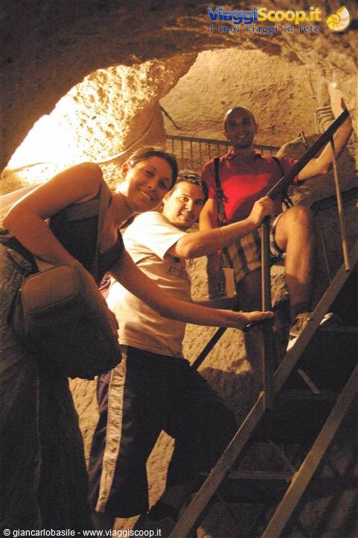 Tourists on metal staircase inside rock-hewn tunnel, warm lighting