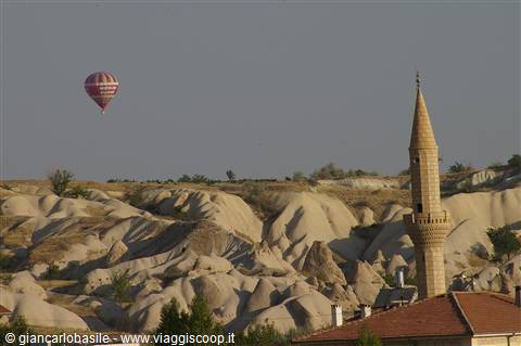 Hot air balloon over volcanic rock formations and a stone minaret, Cappadocia