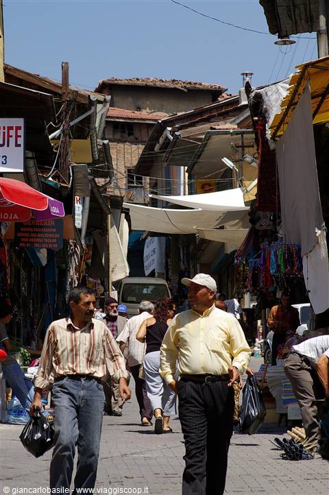 Men carrying shopping bags walk through a market alley shaded by tarps