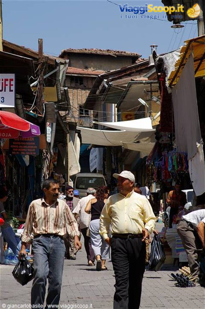 Men carrying shopping bags walk through a market alley shaded by tarps