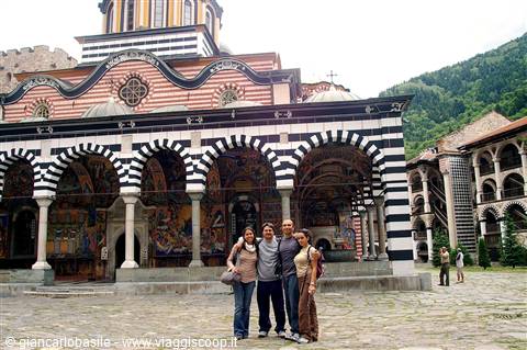 Four friends pose in front of the striped arches of Rila Monastery