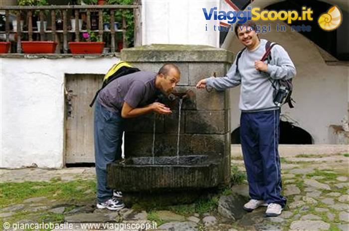 Tourist drinks from an old stone fountain while his friend smiles beside