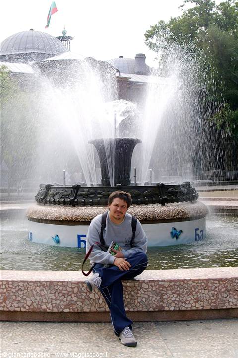 Guy sitting on a fountain edge with water jets, domed mosque behind