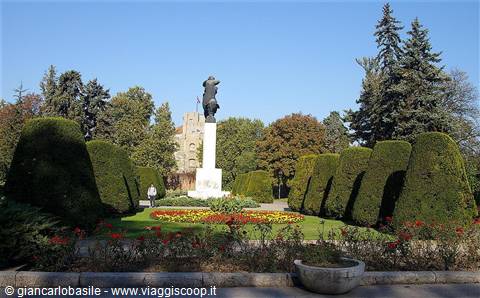 Statue on stone pedestal in Kalemegdan park, trimmed hedges and flowerbeds under blue sky