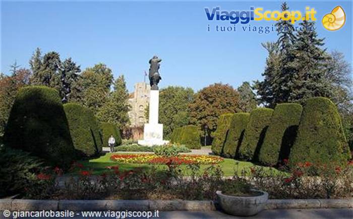 Statue on stone pedestal in Kalemegdan park, trimmed hedges and flowerbeds under blue sky