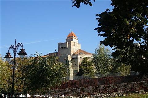 Stone castle with red-roofed tower above brick walls and trees, blue sky