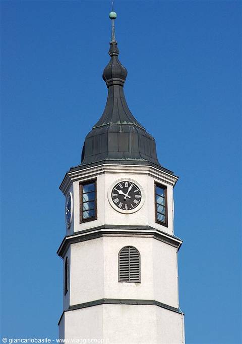 White clock tower with dark dome spire against clear blue sky