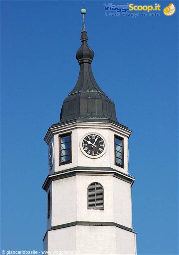 White clock tower with dark dome spire against clear blue sky