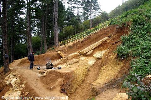 Hiker beside limestone boulders on reddish soil, pine forest along mountain trail