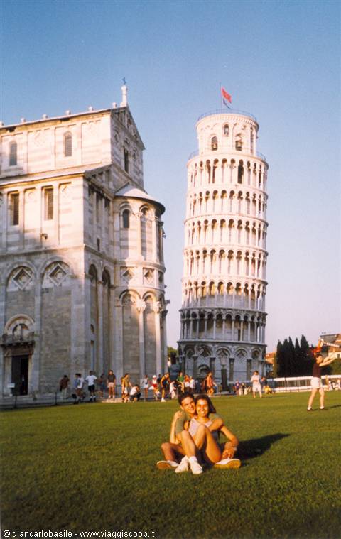 Two girls sitting on the lawn in front of the Leaning Tower of Pisa