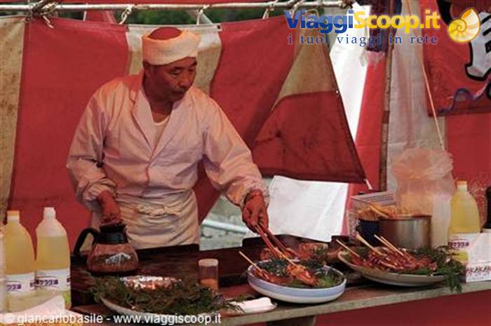 Cook in white headband grilling chicken skewers at a festival food stall