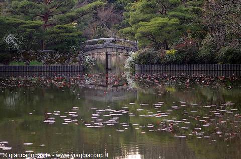 Stone arched bridge over pond with fallen leaves, Kyoto gardens