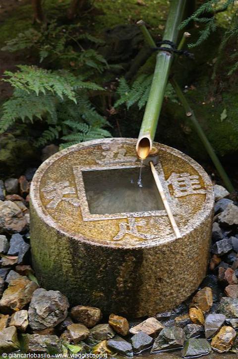 Stone tsukubai basin with bamboo pipe pouring water, carved kanji, mossy garden