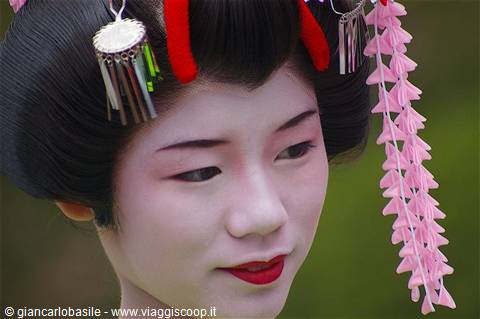 Portrait of a maiko with white makeup, black hair and pink kanzashi