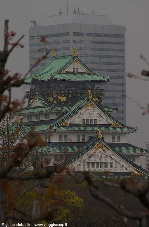 Osaka Castle framed by autumn branches, green roofs and a misty skyscraper