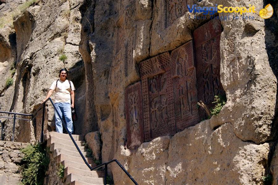 Woman on stone stairs beside khachkar carvings in rock, Geghard monastery