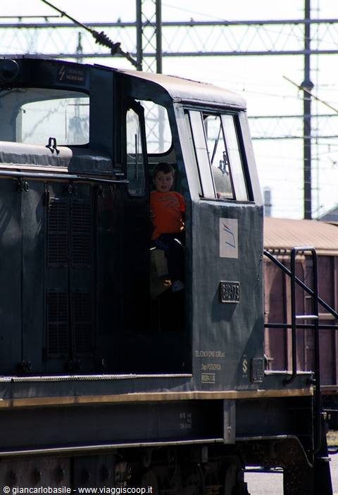 Child in orange shirt looking out from the cab of an old green locomotive