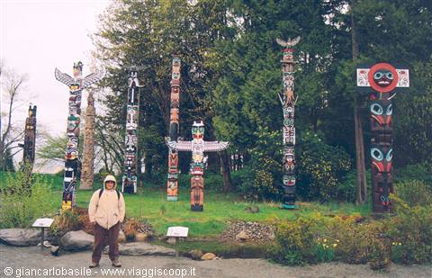 Hooded tourist standing among tall painted totem poles in a park