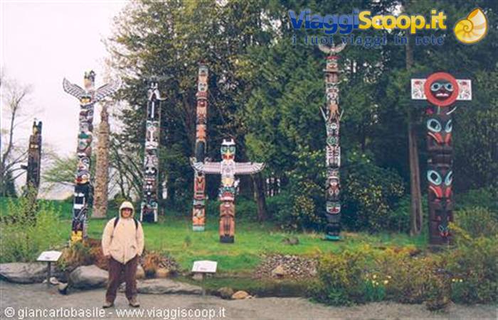 Hooded tourist standing among tall painted totem poles in a park