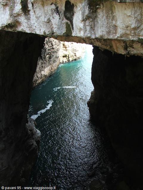 From inside a dark limestone sea cave, turquoise water visible between rocky cliffs