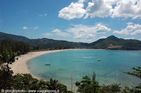 Boat on tropical beach, turquoise water and green hills under white clouds