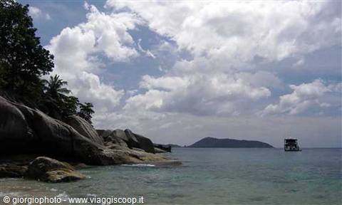 Granite boulders and palms on the beach, anchored boat in front of the island
