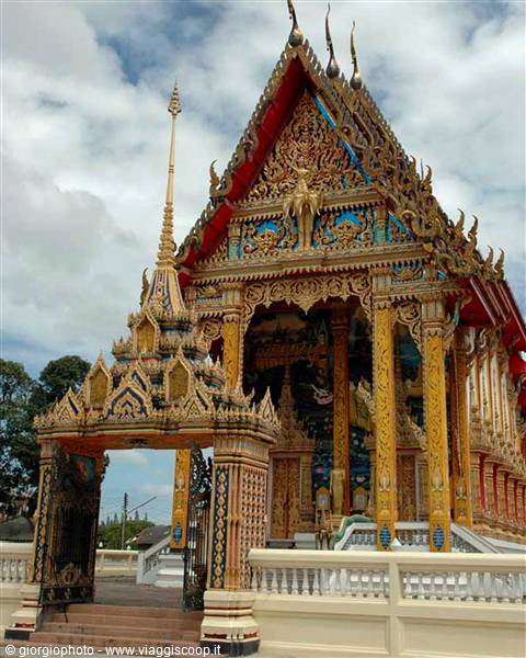 Ornate Thai Buddhist temple with golden columns and decorated gate under cloudy sky