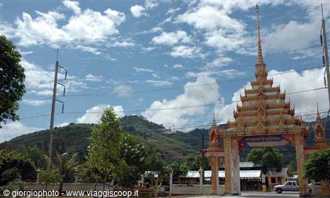 Golden Thai temple gateway under cloudy sky, green hills in the background
